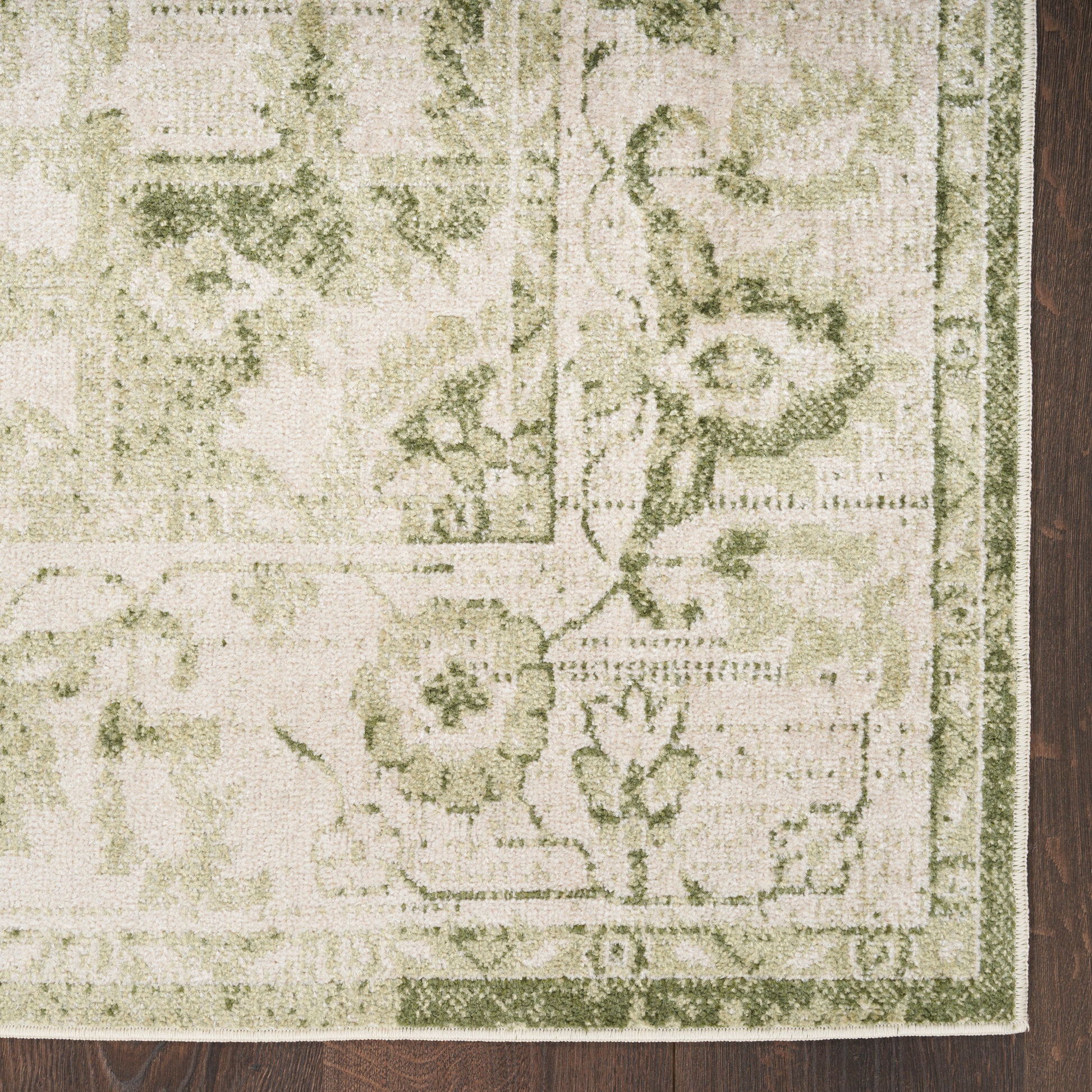 Beige and sage green floral area rug with decorative border, rectangular, on dark wood floor.