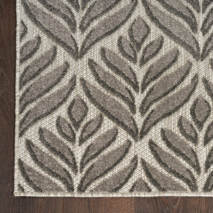 Gray and taupe leaf-pattern area rug on dark wood floor; woven texture with beige base and fringed edge.