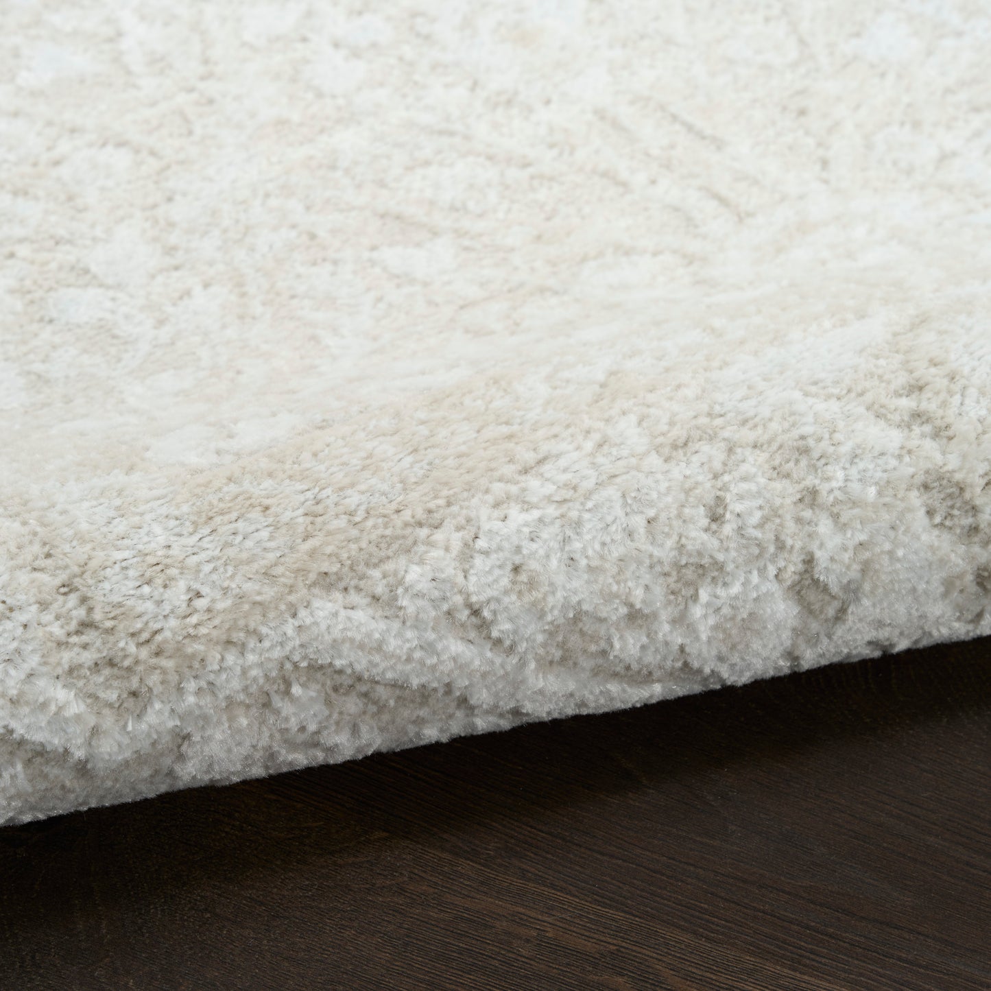 Cream shag rug with plush high-pile texture, folded edge on dark wood floor.