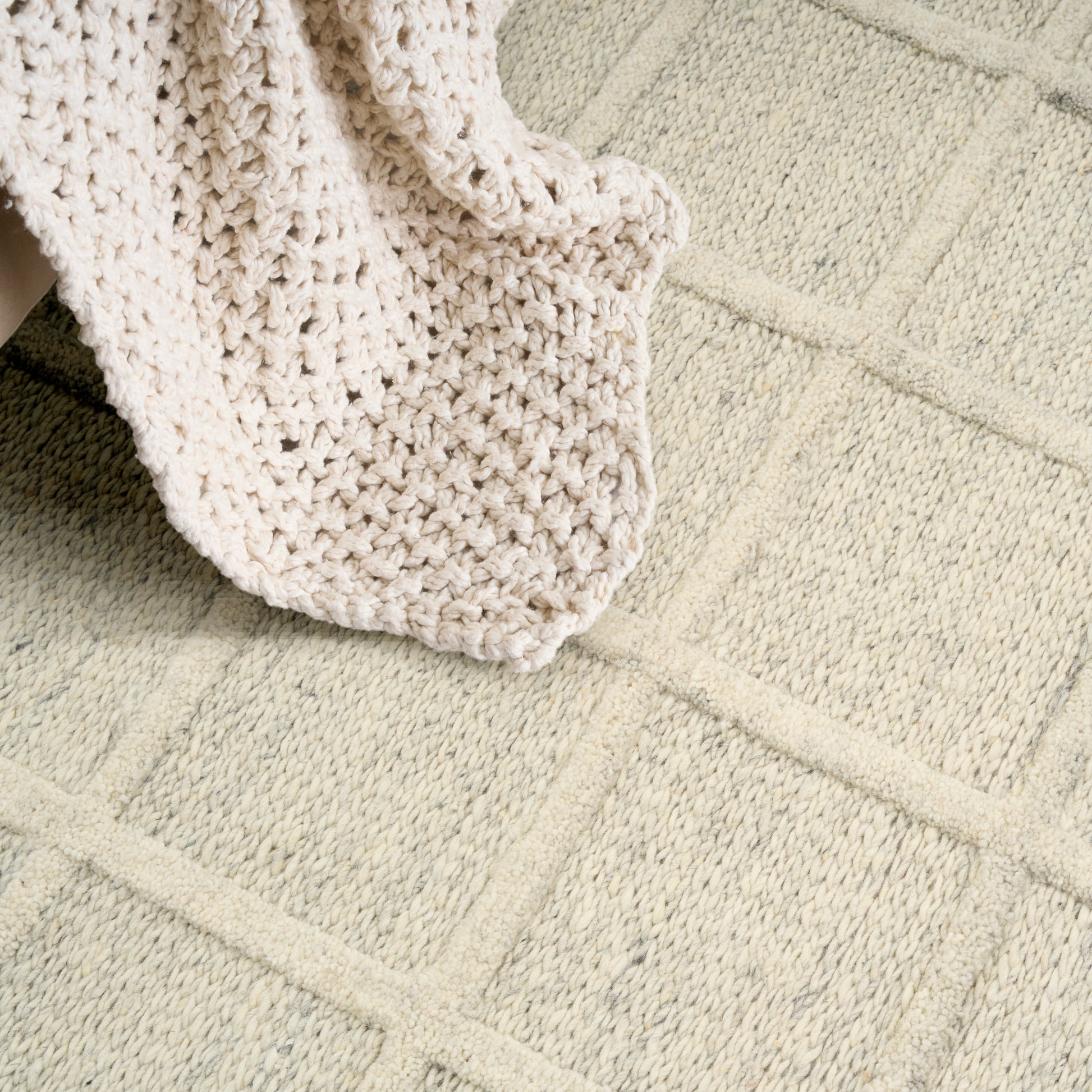 Cream chunky knit blanket draped over a light beige rug with square geometric pattern.