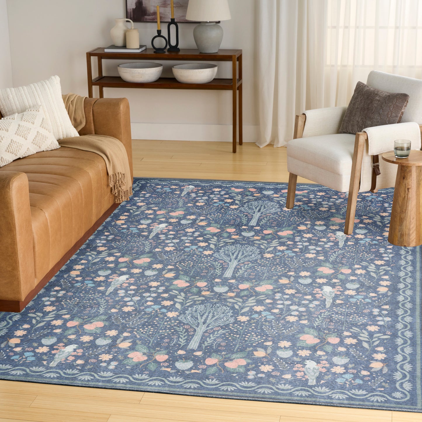 Blue patterned area rug with botanical tree motif and pink accents in a light-wood living room.
