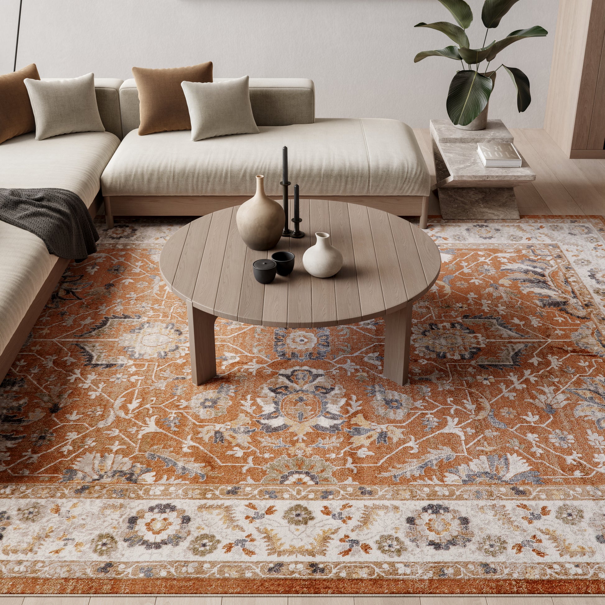 Round wooden coffee table with ceramic vases and candle holder on an orange-and-cream oriental rug beneath a beige sectional.