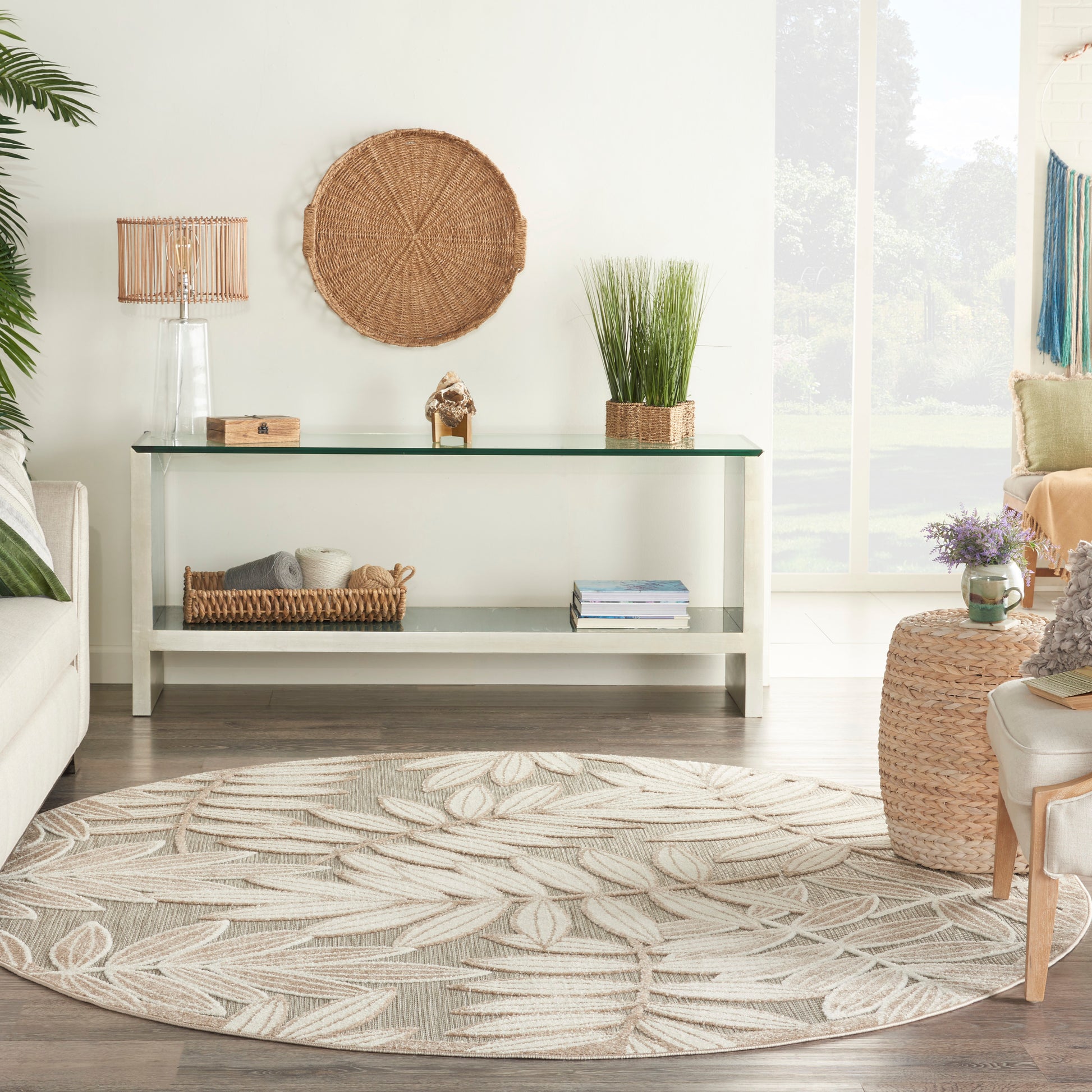 Coastal living room with glass-top white console, woven wall art, potted grasses, wicker baskets, and beige leaf-pattern rug