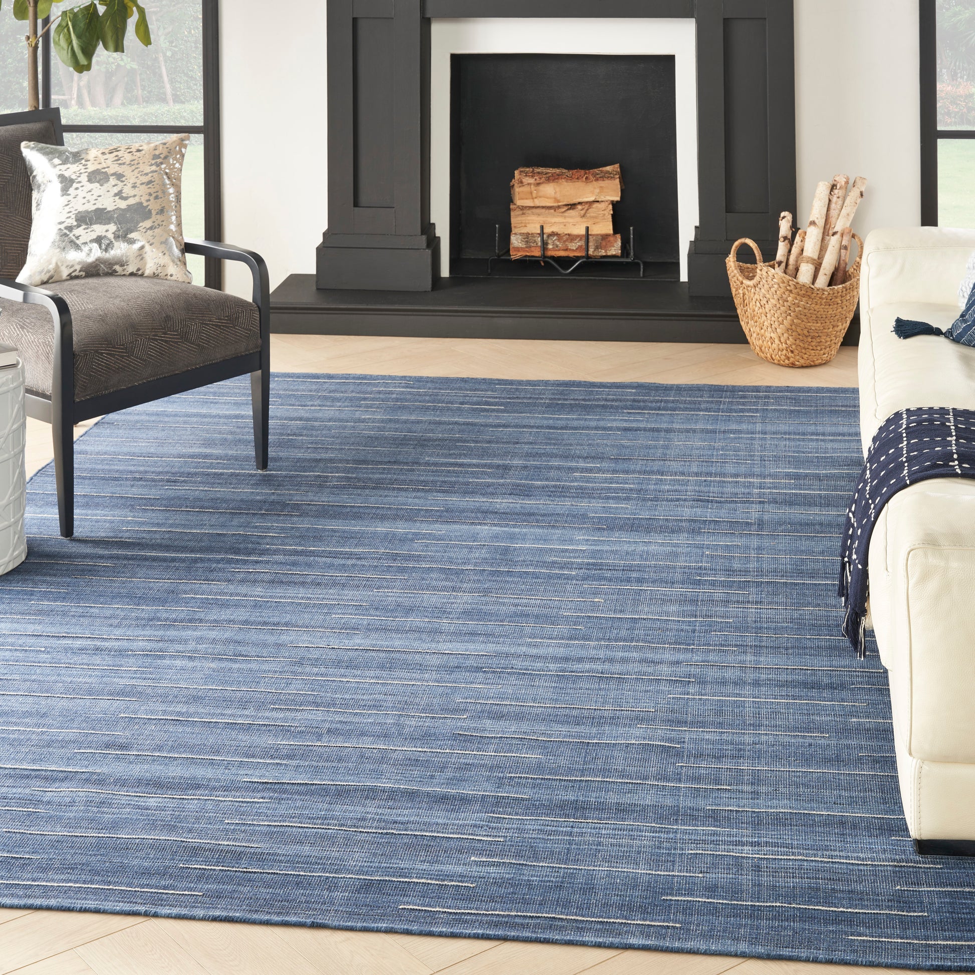Blue striped area rug in a modern living room with a black fireplace, gray chair, cream sofa, and a log basket.