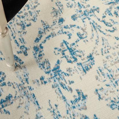 Close-up of a silver metal chair leg on a cream rug with blue damask pattern.