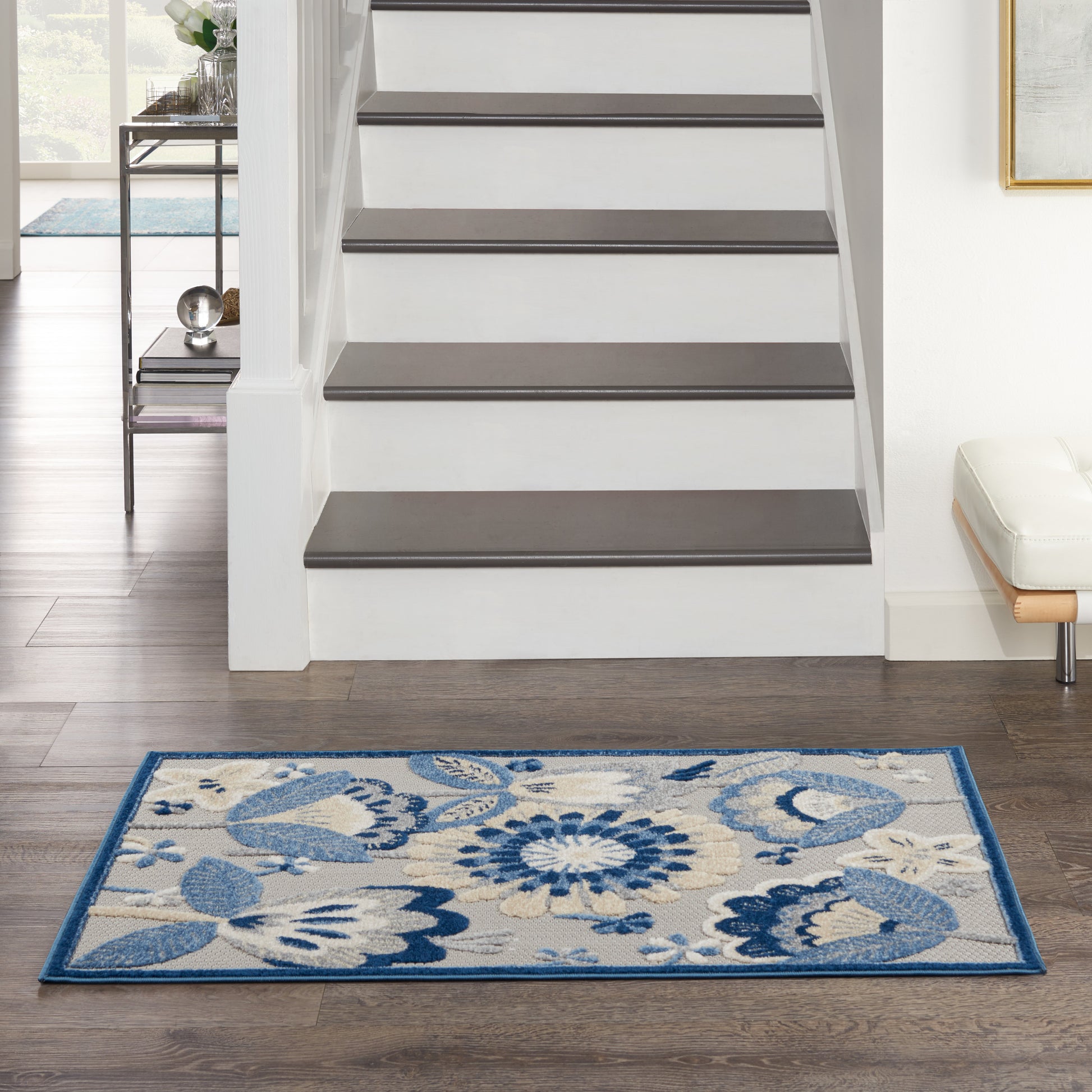 Rectangular blue and cream floral area rug with a dark blue border on dark hardwood beside a modern staircase.