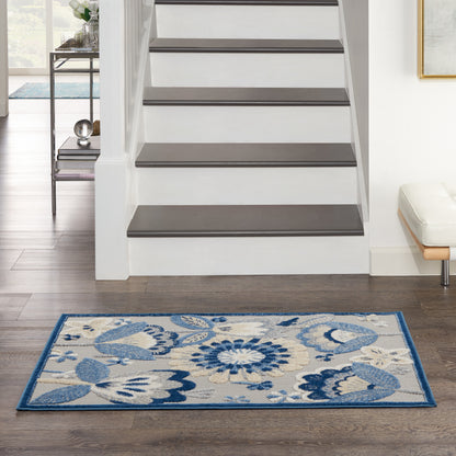 Rectangular blue and cream floral area rug with a dark blue border on dark hardwood beside a modern staircase.