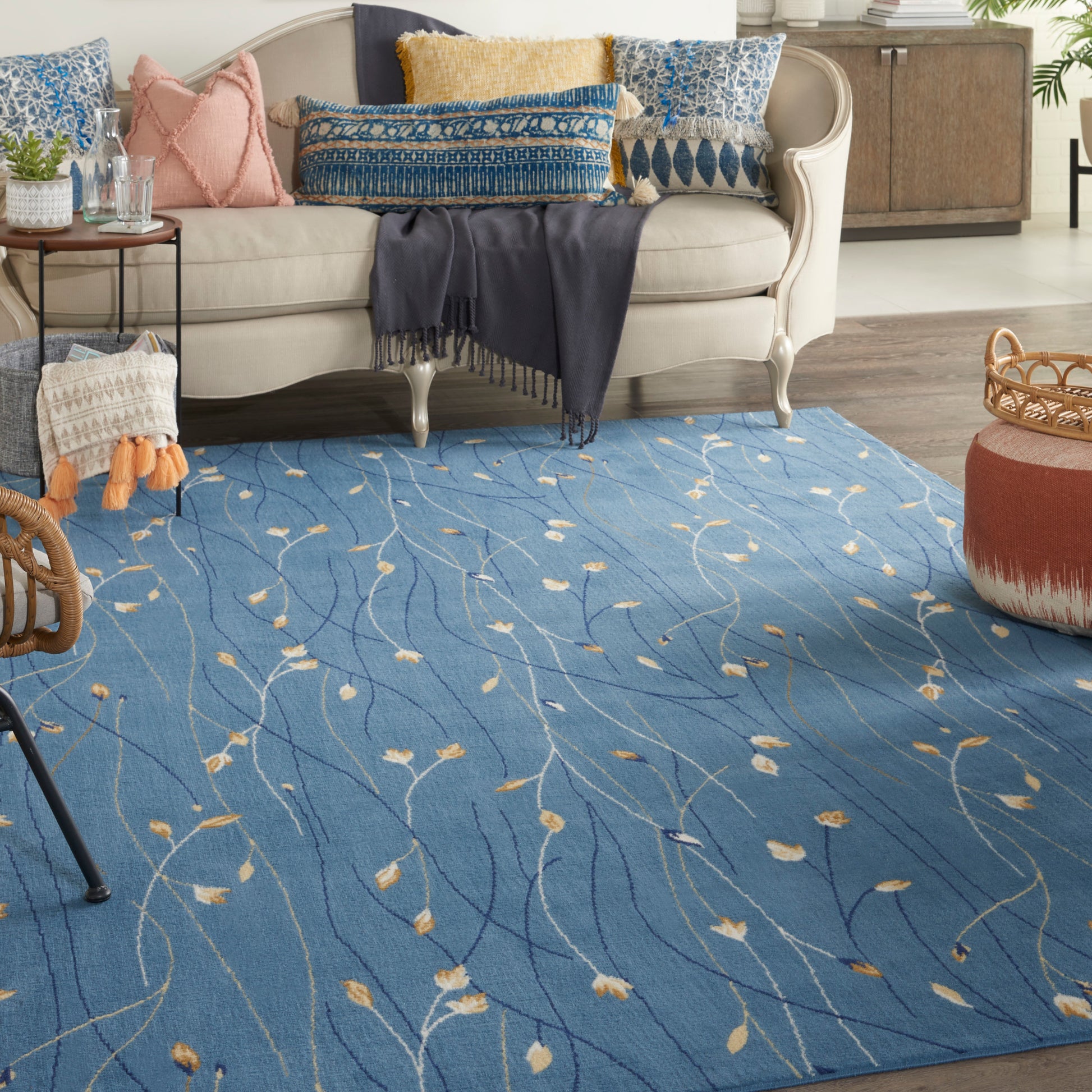 Blue area rug with cream leaf pattern under a beige sofa; coastal cushions, navy throw, wicker basket, round ottoman.