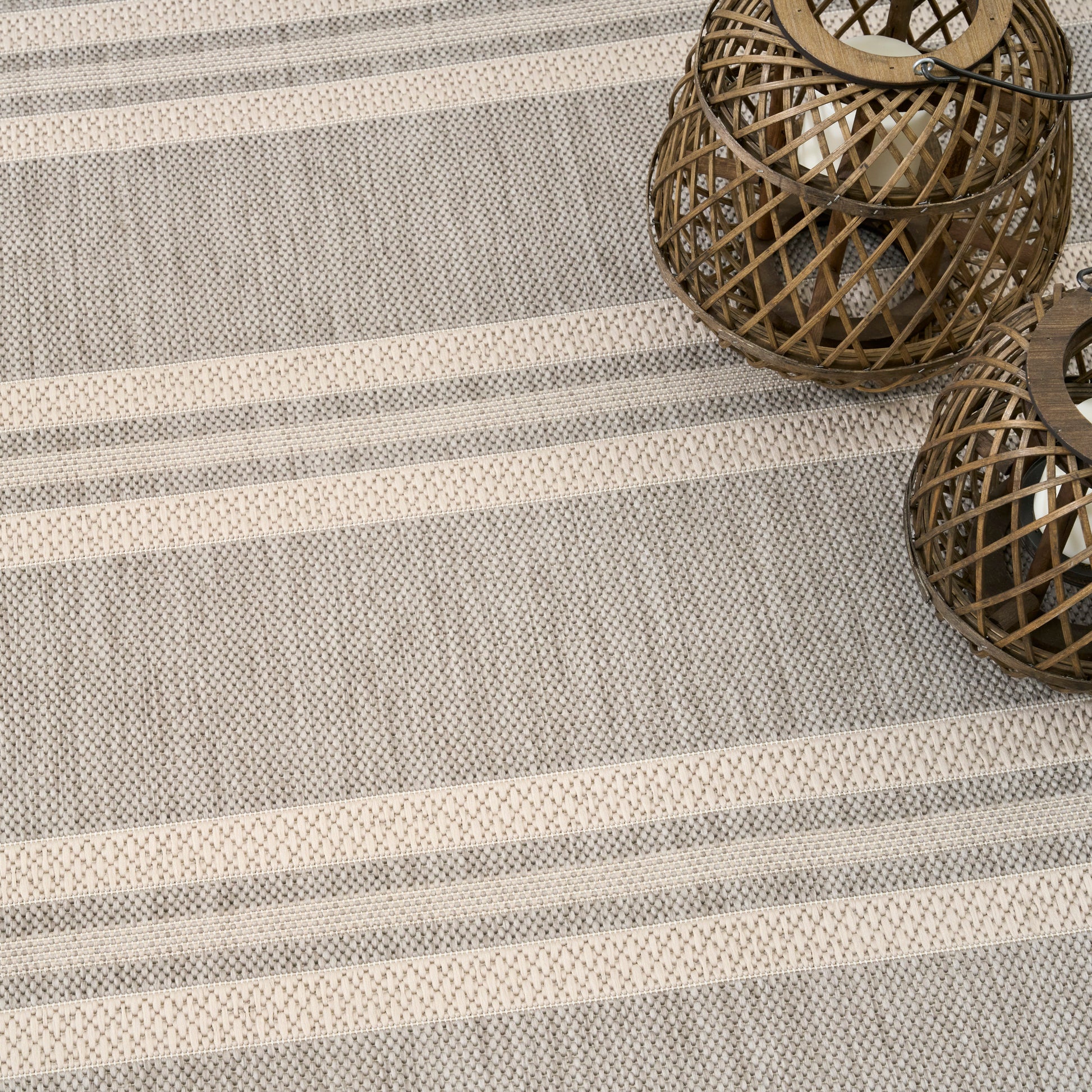 Beige and gray striped woven rug with a textured pattern; two brown wicker lanterns in the corner.