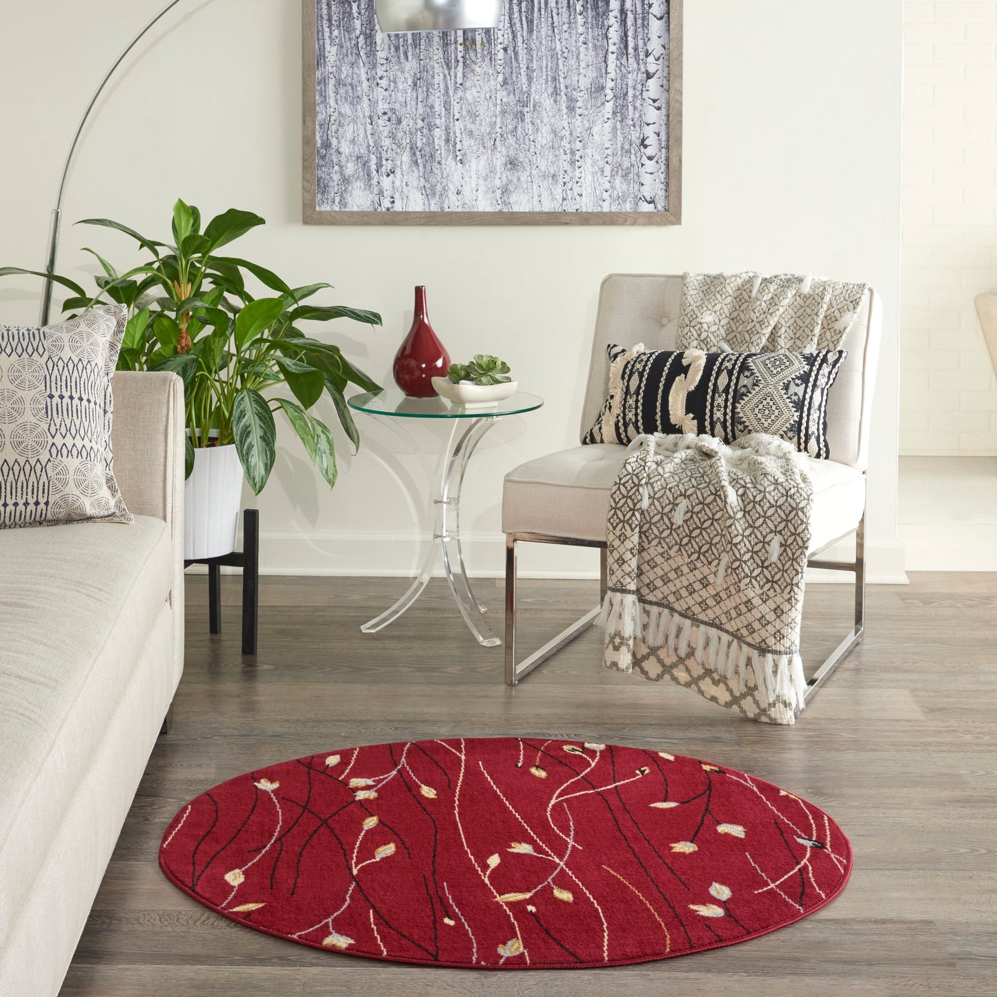 Red round rug with cream vine pattern; modern living room with beige sofa, patterned cushions, glass side table, and plant.