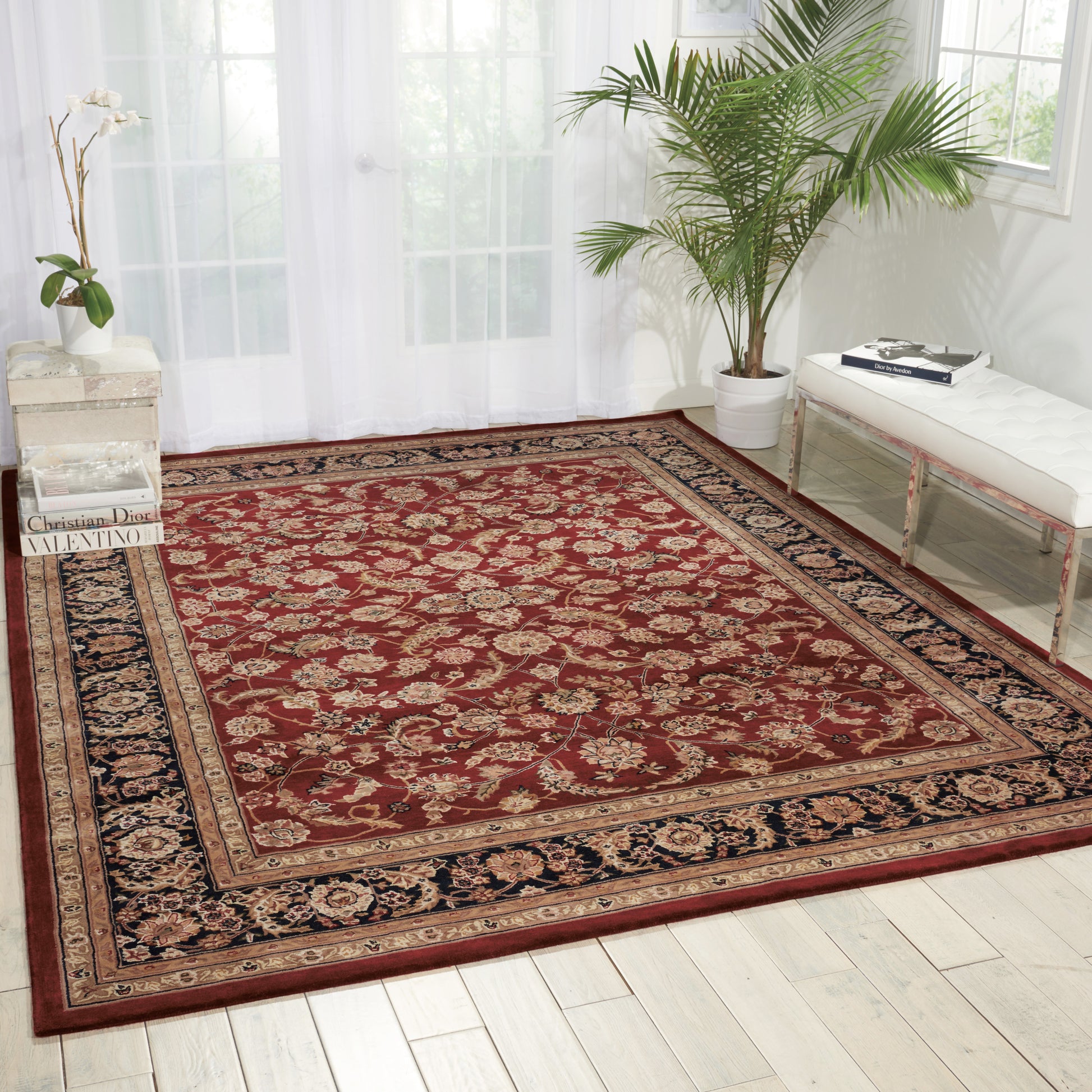 Red Persian-style area rug with ivory floral medallions and a navy border on a light wooden floor in a bright room.