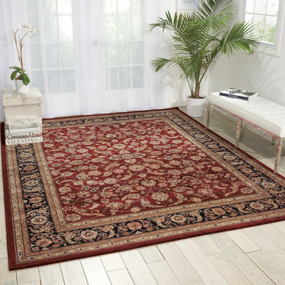 Red Persian-style area rug with ivory floral medallions and a navy border on a light wooden floor in a bright room.