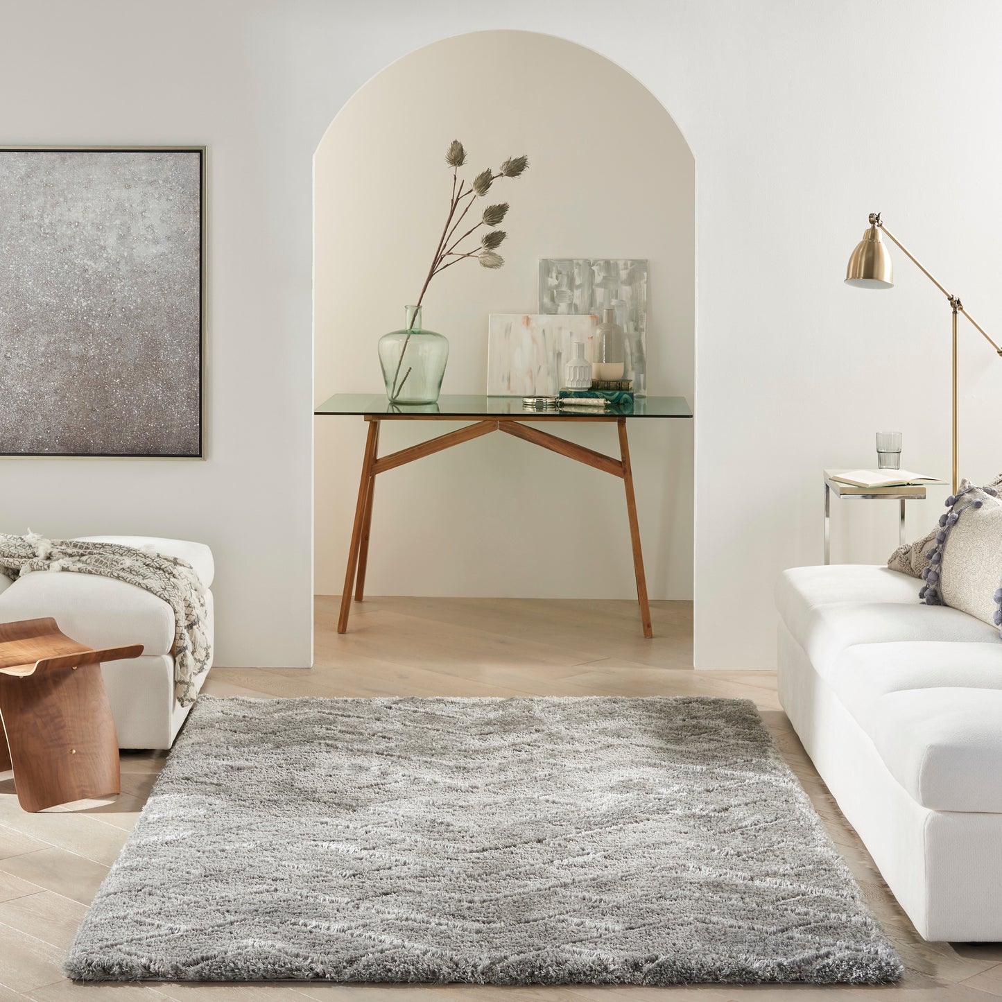 Soft gray shag rug anchors a bright modern living room with white sofa, arched niche glass-top table, vase, and art prints.
