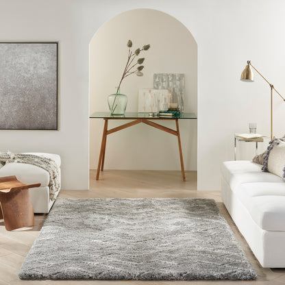 Soft gray shag rug anchors a bright modern living room with white sofa, arched niche glass-top table, vase, and art prints.