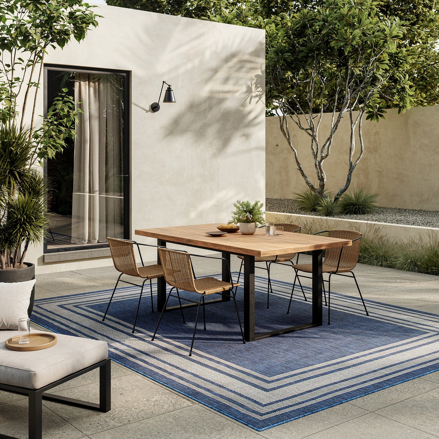 Blue striped rug on a patio with a beige wall, glass door and garden plants.
