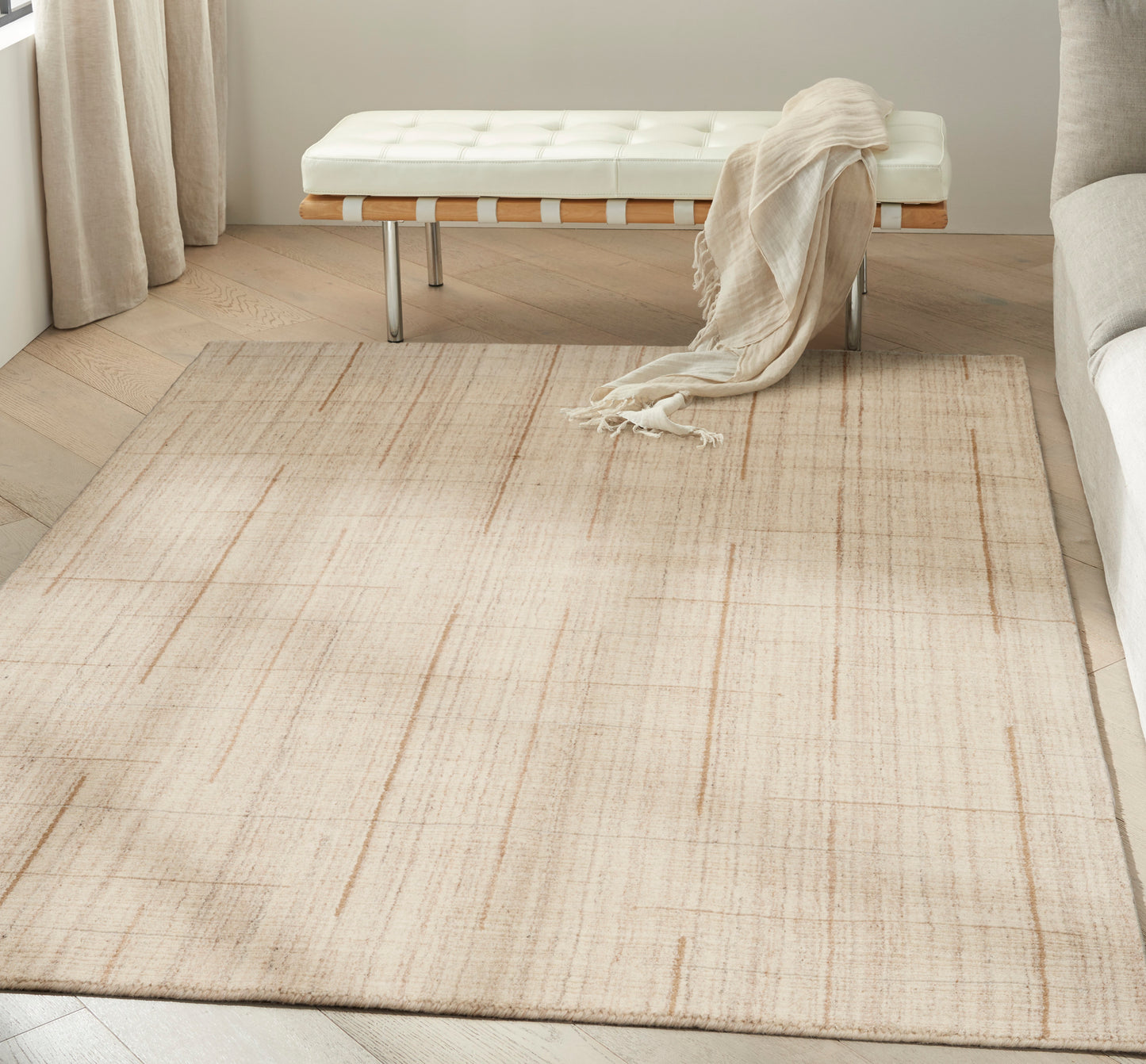 Beige flat-weave area rug with a subtle linear pattern in a modern living room with a white tufted bench and cream throw.