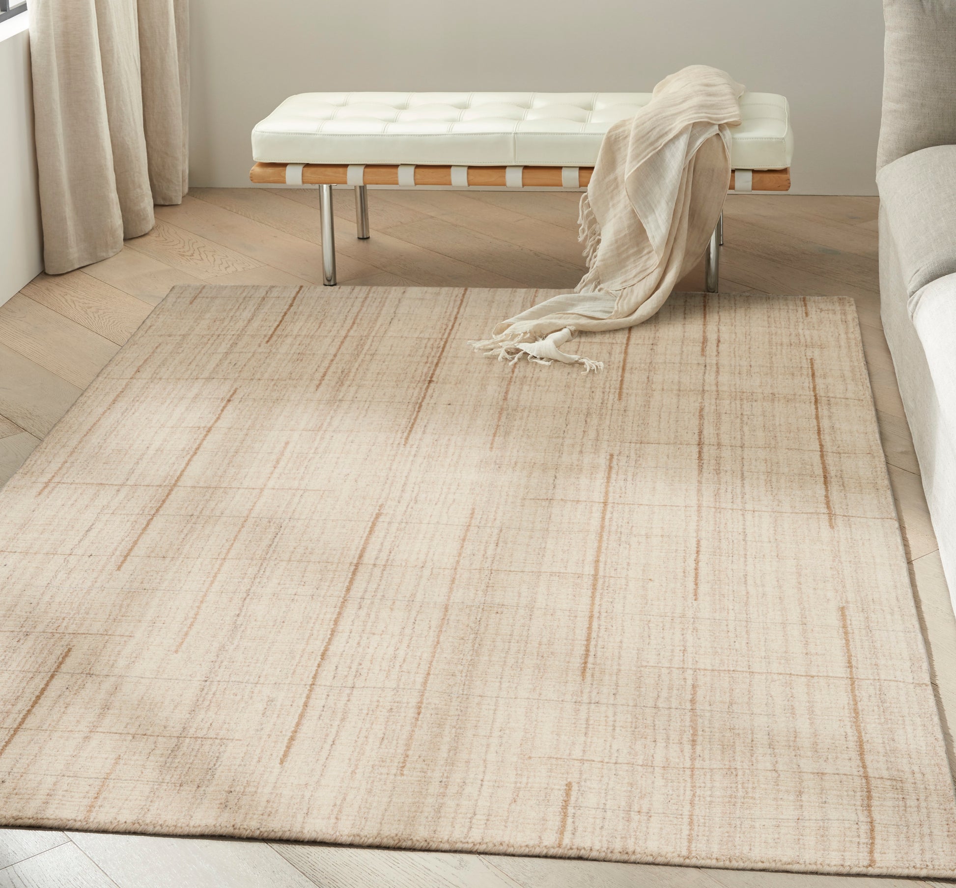 Beige flat-weave area rug with a subtle linear pattern in a modern living room with a white tufted bench and cream throw.