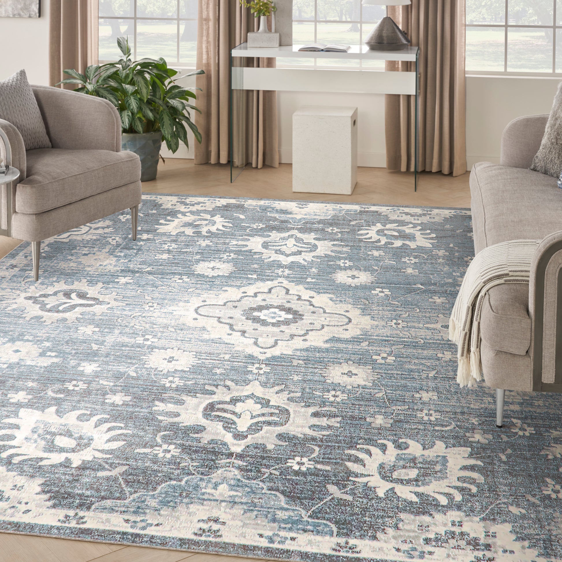 Blue and ivory ornate patterned area rug in a living room with beige sofas, a potted plant, and a white console desk.