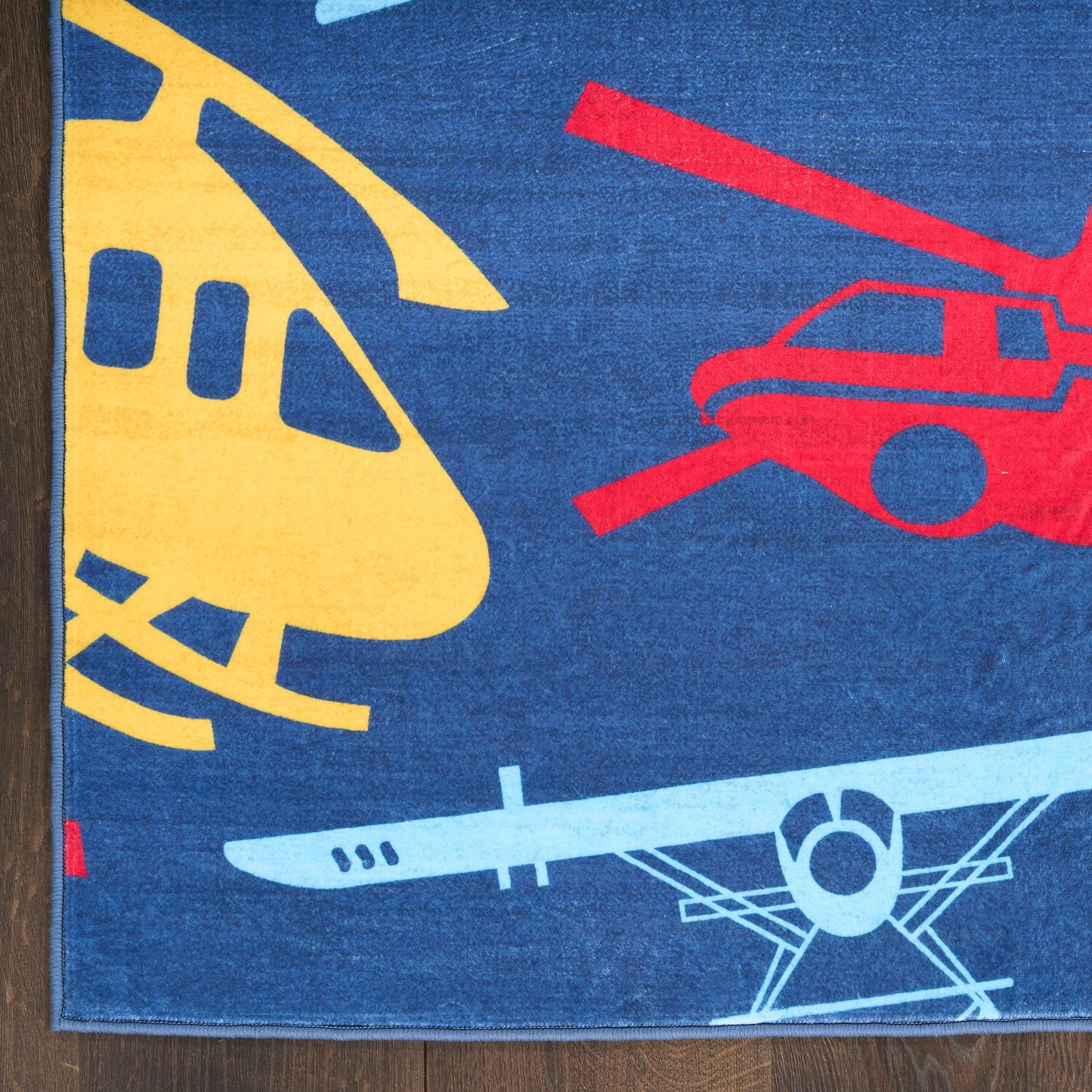 Blue woven rug featuring yellow helicopter, red car, and light-blue airplane silhouettes; kid-friendly transport print.
