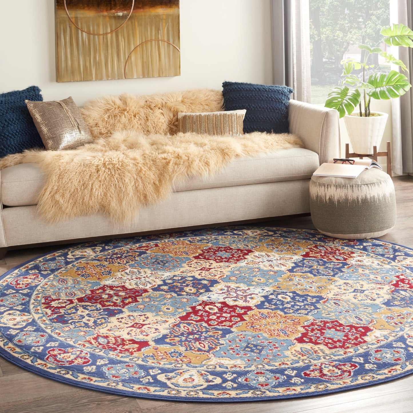 Round ornate area rug in blue, red and ivory with floral motifs; beige sofa with tan faux fur throw and navy cushions.