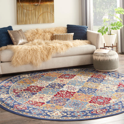 Round ornate area rug in blue, red and ivory with floral motifs; beige sofa with tan faux fur throw and navy cushions.