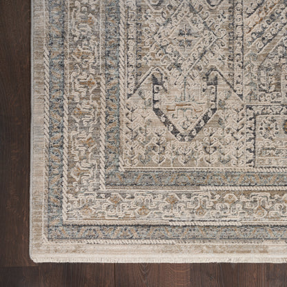 Rectangular beige area rug with blue/gray ornate geometric border on a dark wood floor.