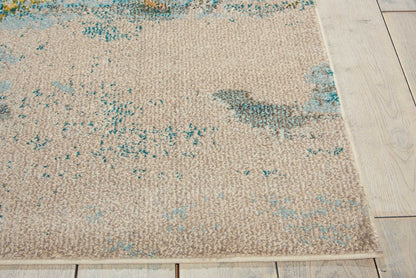Beige rectangular flat-weave rug with turquoise and teal abstract pattern on light wooden floor.