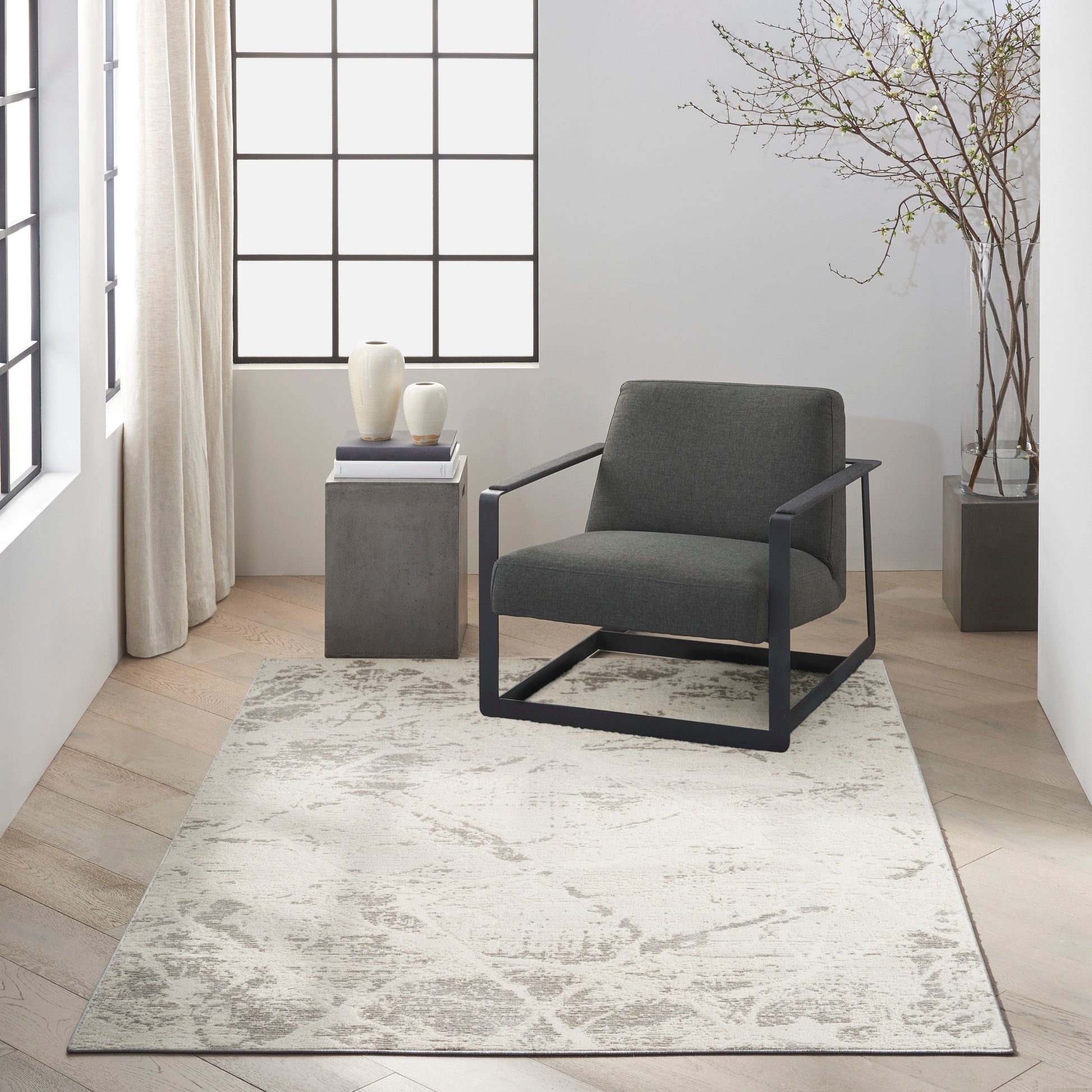 Light patterned rug in a modern living room corner with a dark gray armchair and black metal frame, grid window.