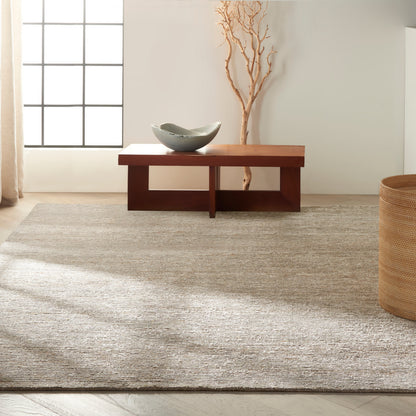 Rectangular rug in a neutral living room; visible elements include a dark wood coffee table with open lower shelf, a gray ceramic bowl, and dried branch decor.
