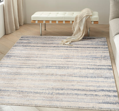 Large cream-blue striped area rug on light wood floor, with a white tufted bench and beige throw.