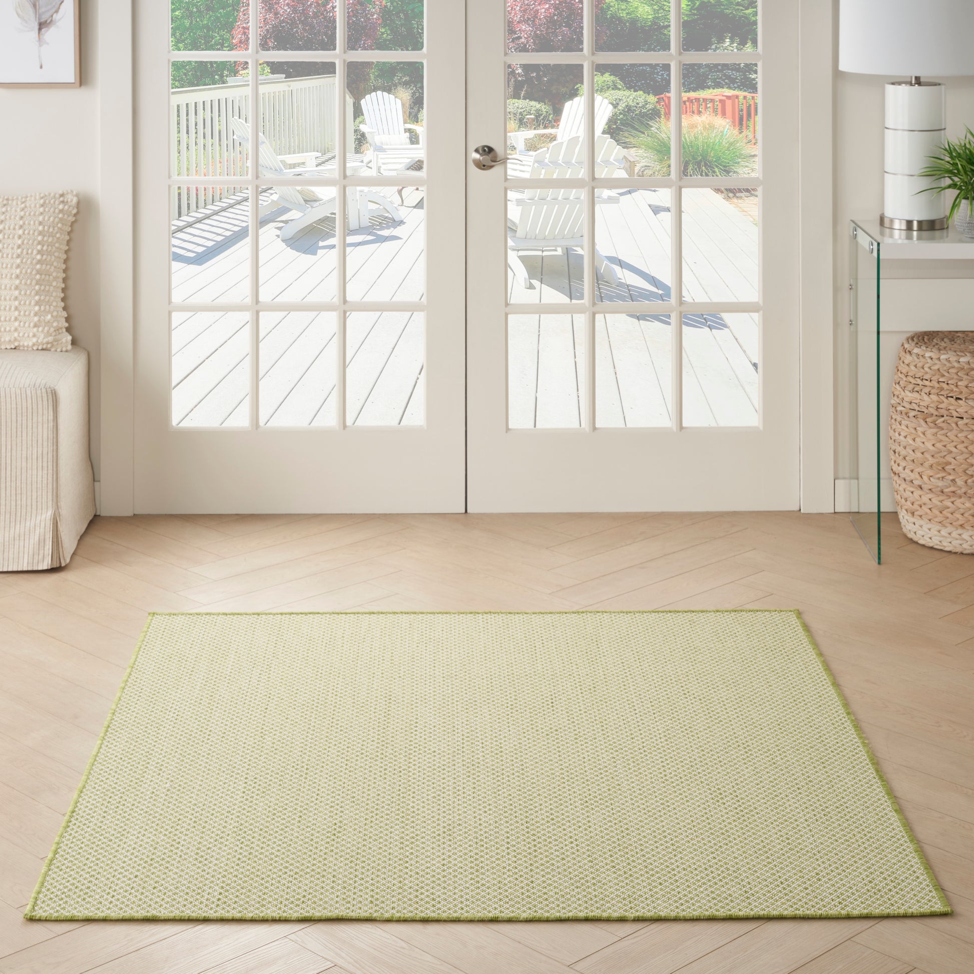 Rectangular light olive-green area rug with lime border in a bright living room by glass doors.