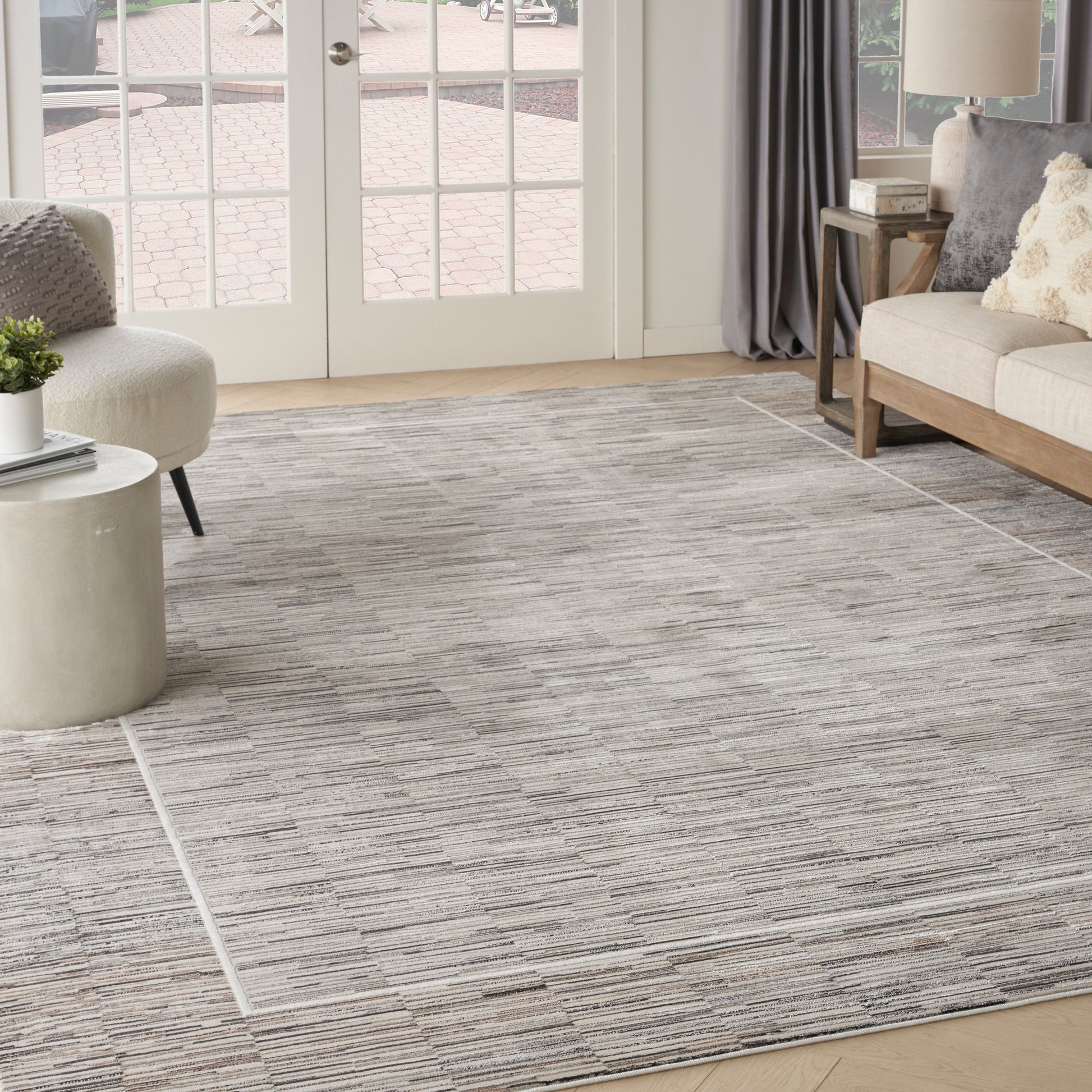 Living room with a gray-striped area rug, beige sofa, round concrete side table, and glass French doors.