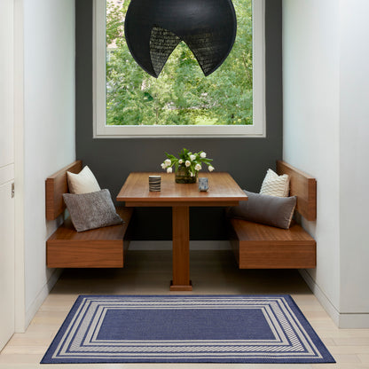 Wood dining nook with built-in benches, square pedestal table, gray cushions, blue striped rug, black dome pendant light.