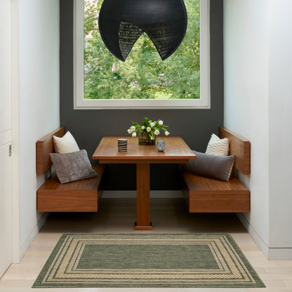 Wooden corner dining nook with L-shaped benches around a square table, black pendant light, window garden view, cushions, and a green geometric rug.
