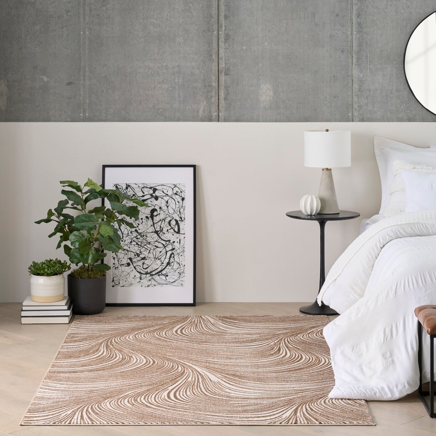 Modern bedroom with gray concrete wall, white bedding, black-framed art, potted plant, round black side table and white lamp.