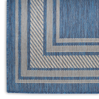Close-up of a blue woven rug with white and beige stripes forming layered square borders; denim-textured textile.