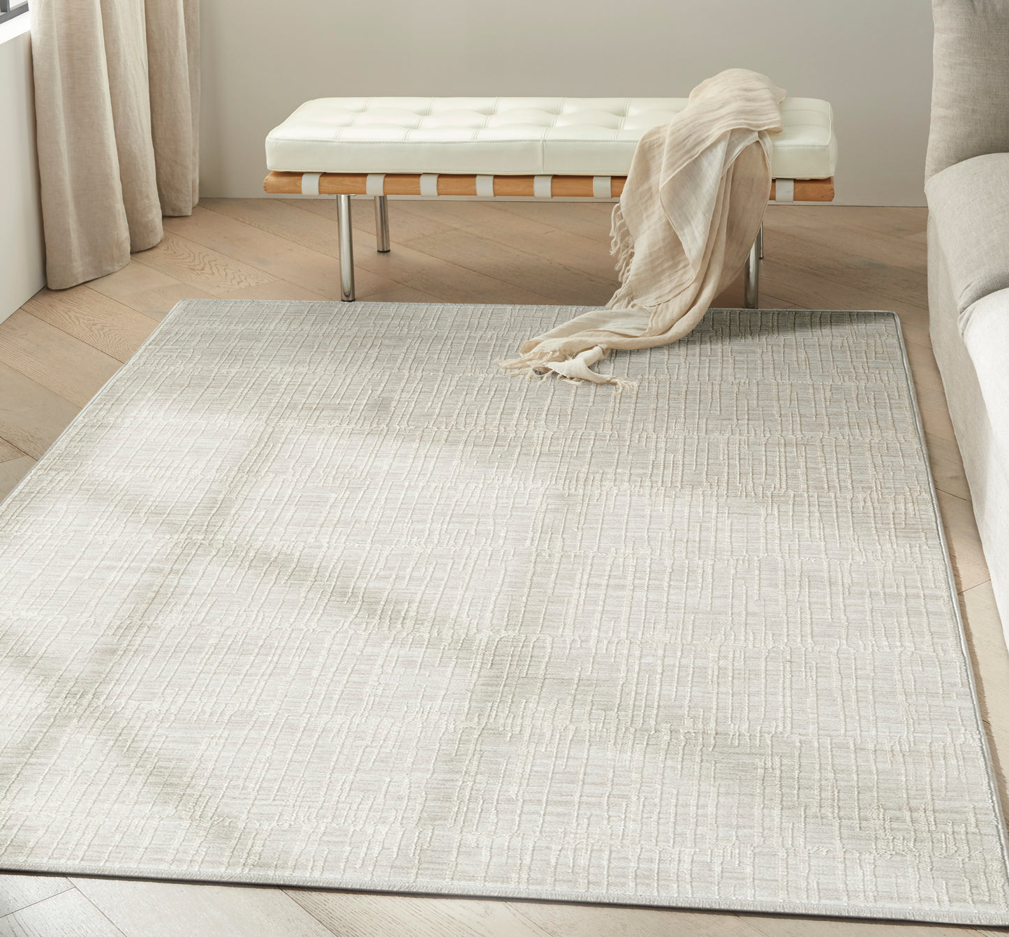 Rectangular light gray textured rug in a neutral living room with a white tufted bench, wooden slats and beige throw.