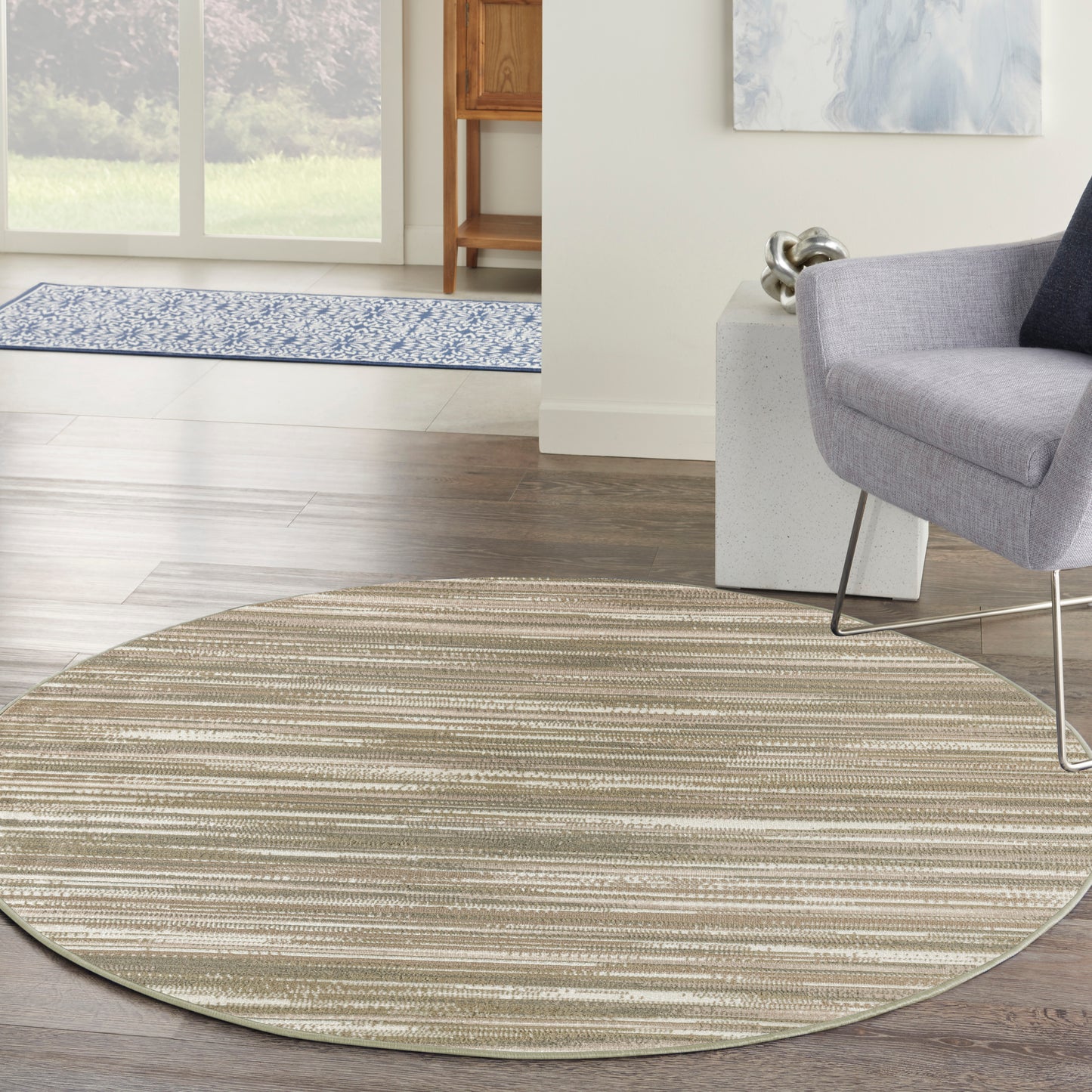 Circular beige striped area rug in a modern living room, under a gray lounge chair on dark wood flooring.