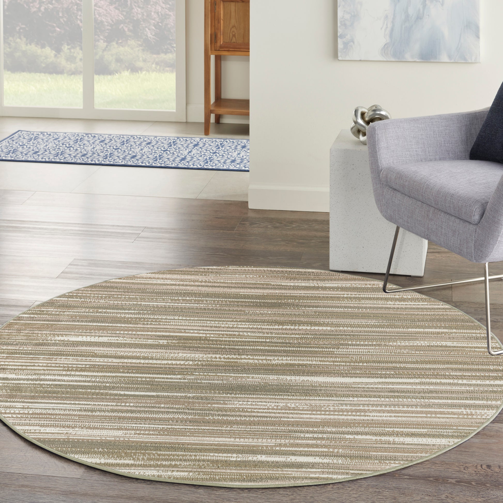 Circular beige striped area rug in a modern living room, under a gray lounge chair on dark wood flooring.