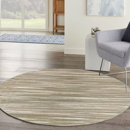 Circular beige striped area rug in a modern living room, under a gray lounge chair on dark wood flooring.
