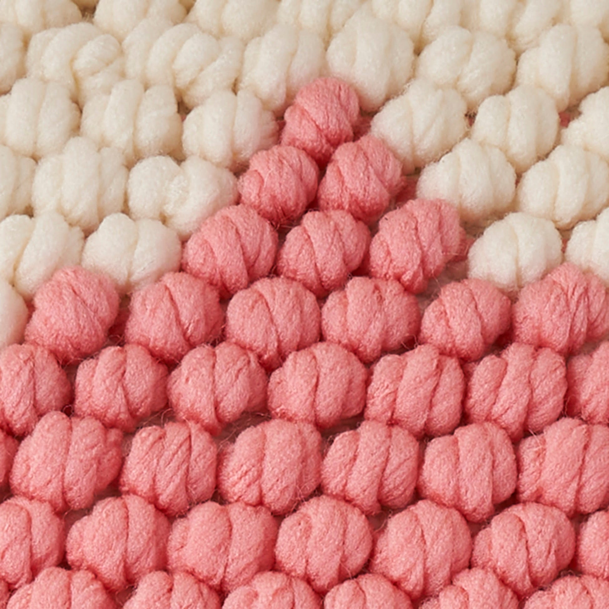 Cream and pink chunky boucle yarn rug with looped bobble tufts; soft, textured home decor.