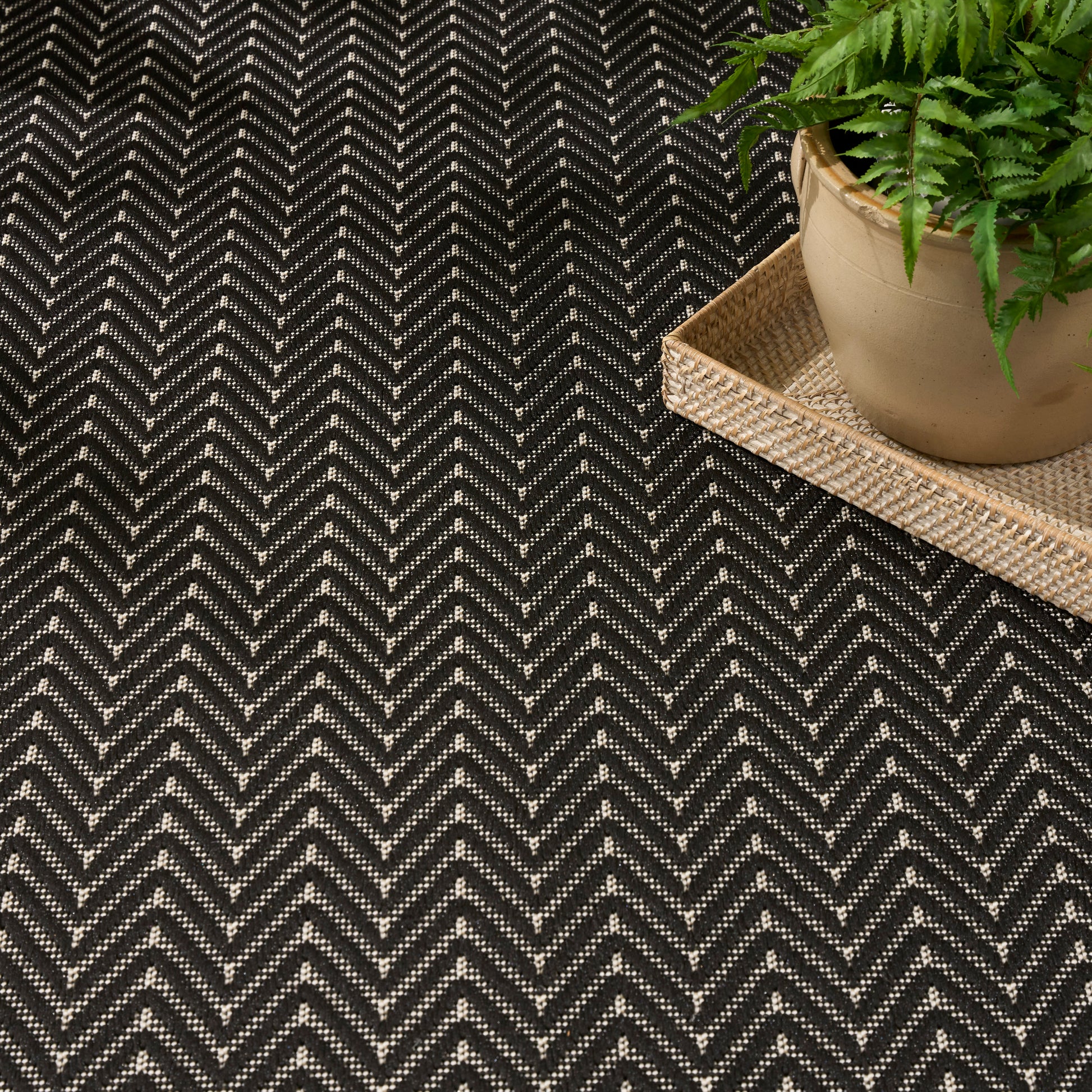 Black and white herringbone rug with a woven natural-fiber tray and potted fern