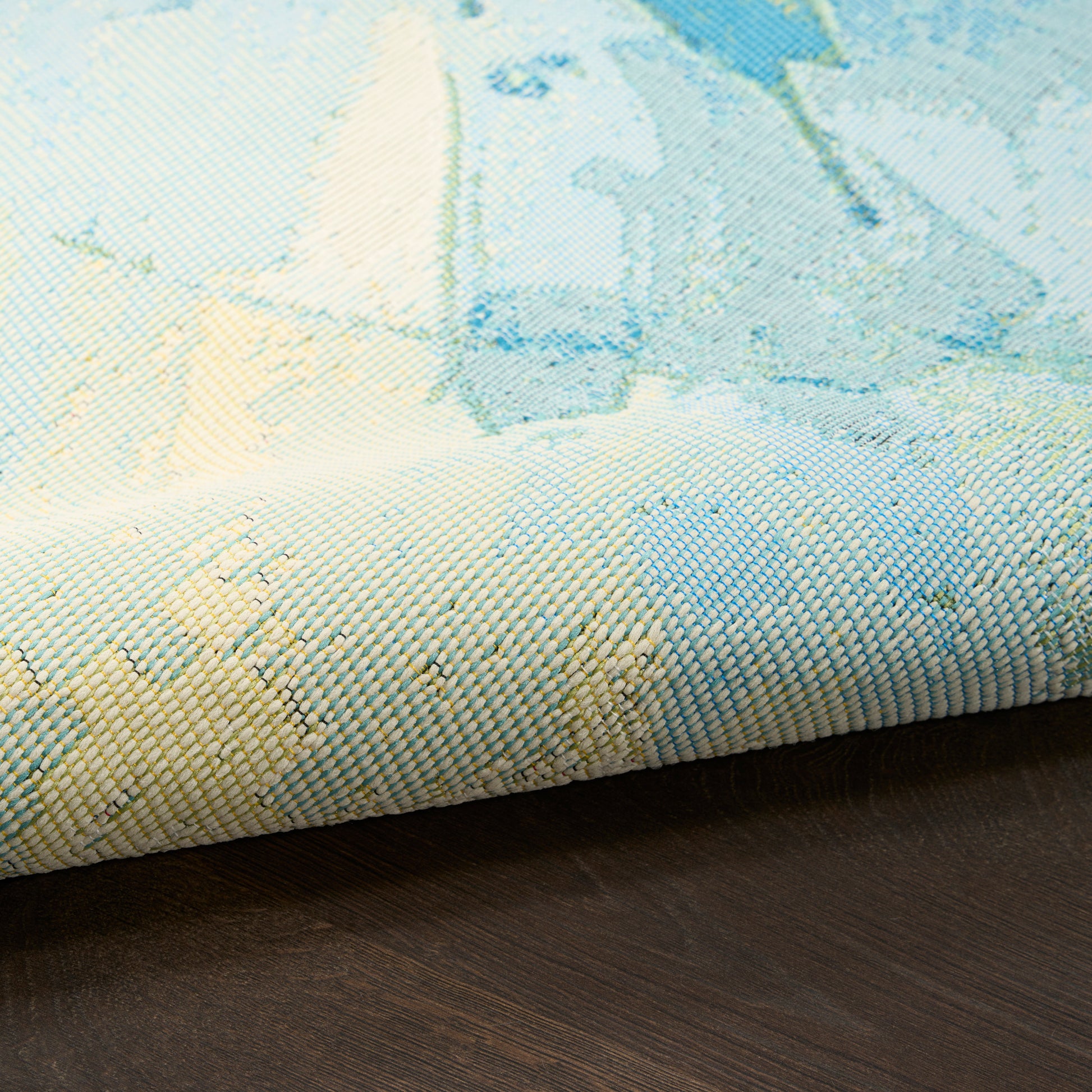 Pastel blue and cream area rug with abstract watercolor pattern, woven texture, folded edge on dark wood floor.