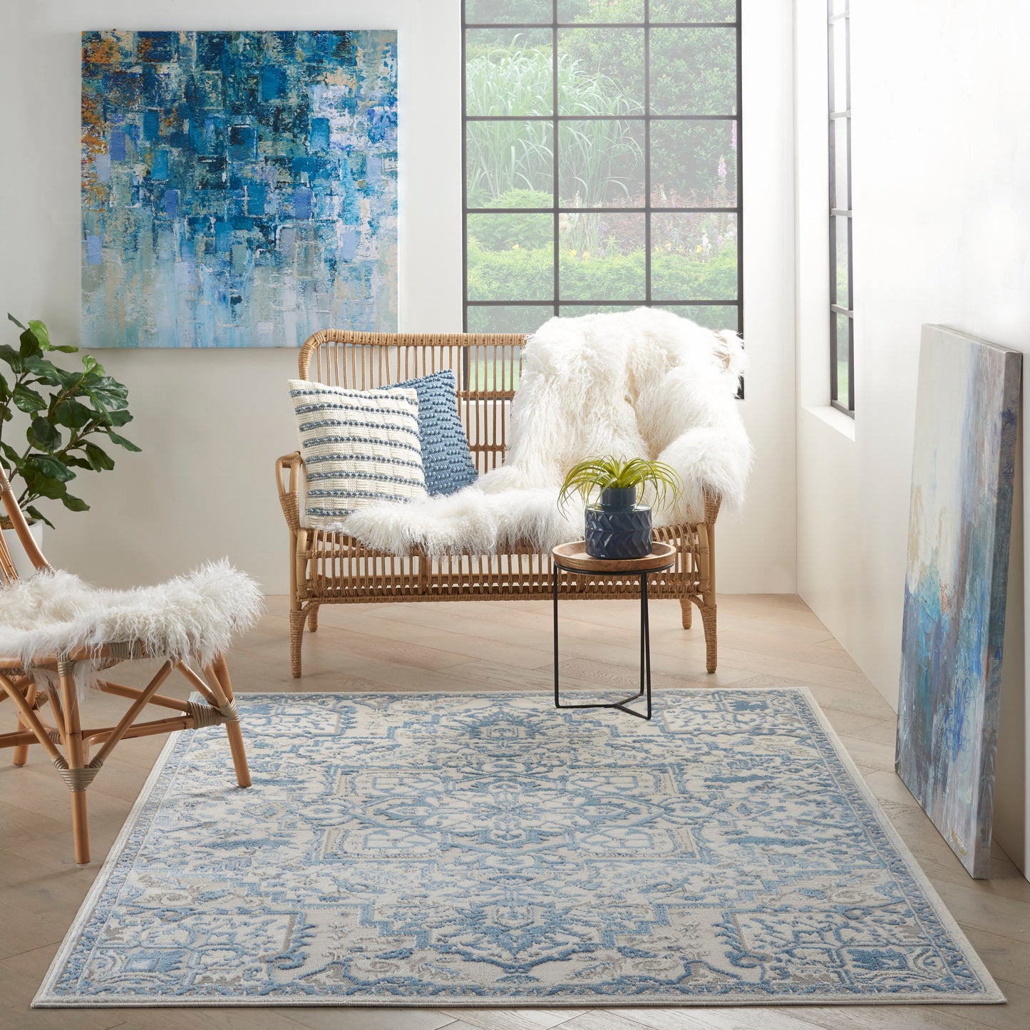 Bright living room featuring a blue patterned rug, rattan seating with faux fur throws, abstract blue wall art, and a large grid window.