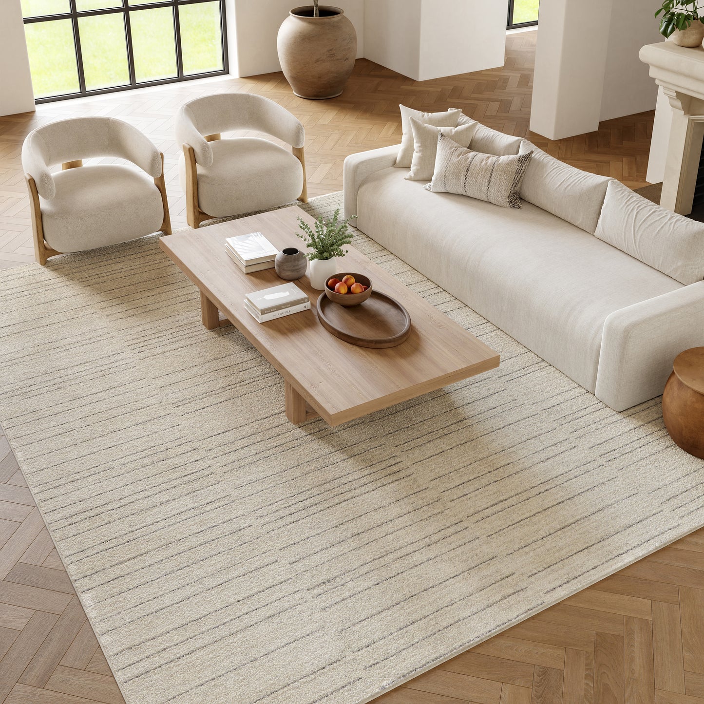 Neutral living room with light wood coffee table, beige striped rug, cream sofa and curved armchairs.
