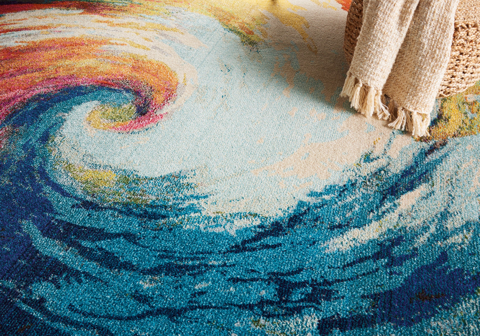 Colorful abstract swirl rug in blues, teals, pinks and yellows with fringe along the edge.