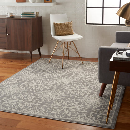 Gray floral-area rug on wood floor with white mid-century chair, gold legs, and a metallic gold throw pillow.