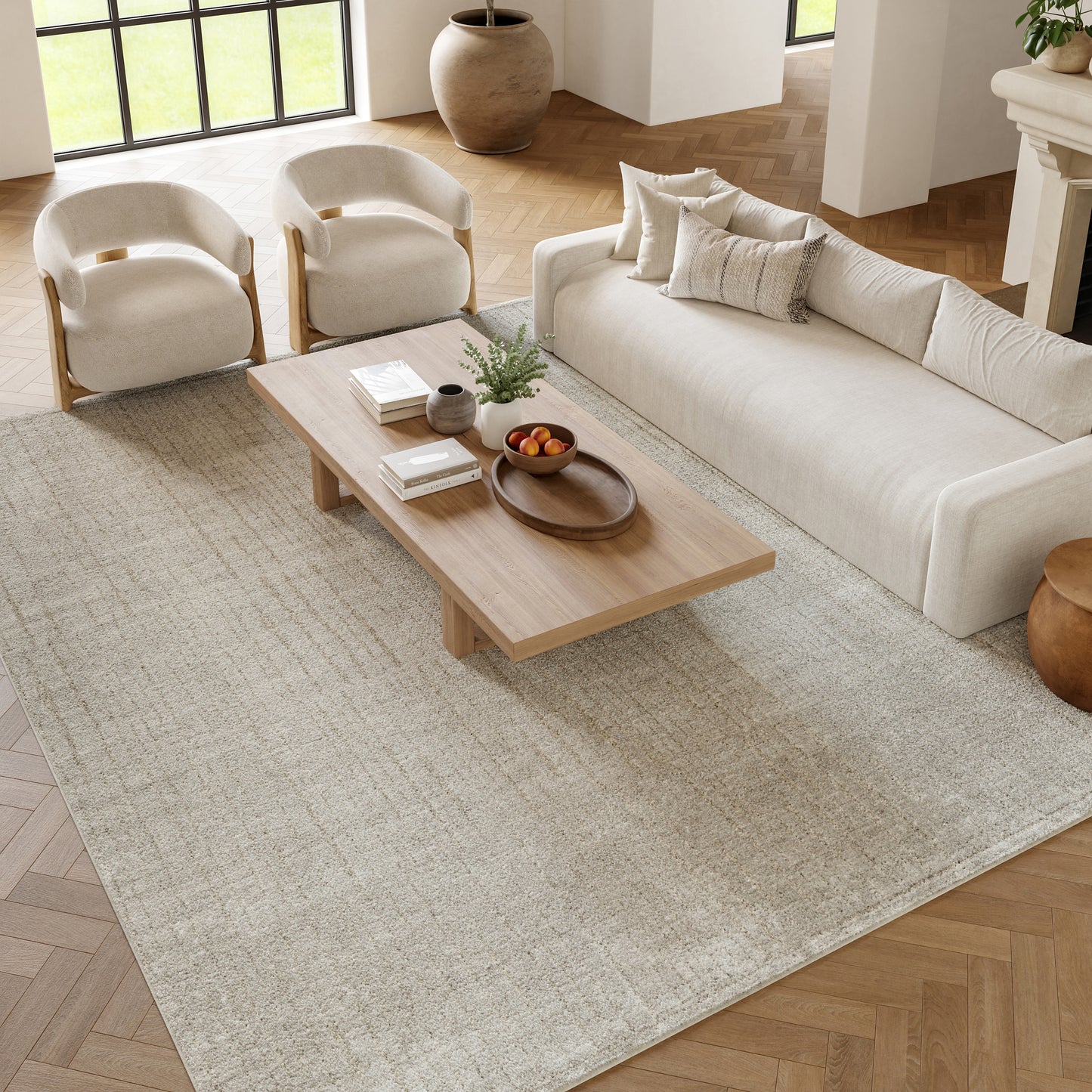 Bright living room with cream sofa, two curved-arm chairs, a low wooden coffee table, beige rug and fruit bowl.
