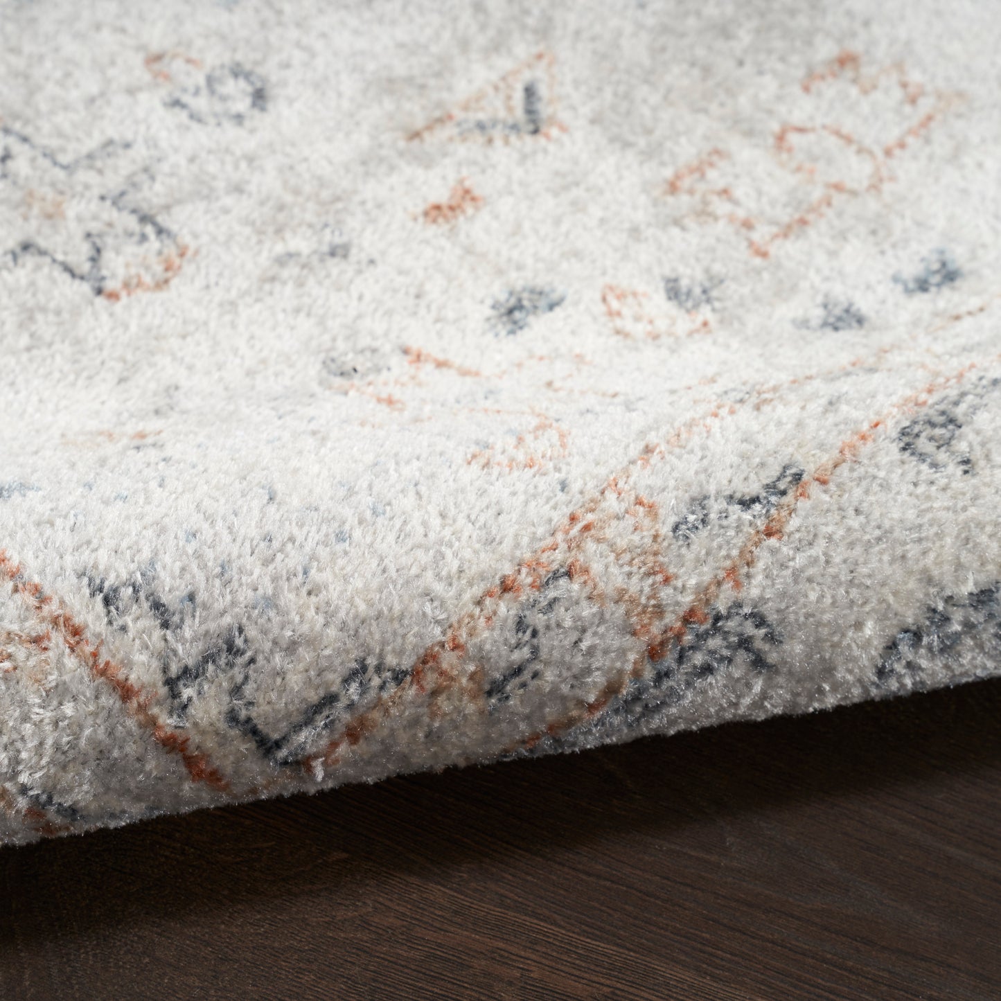Soft light-gray runner rug with orange and navy geometric accents; plush pile on dark wood floor.