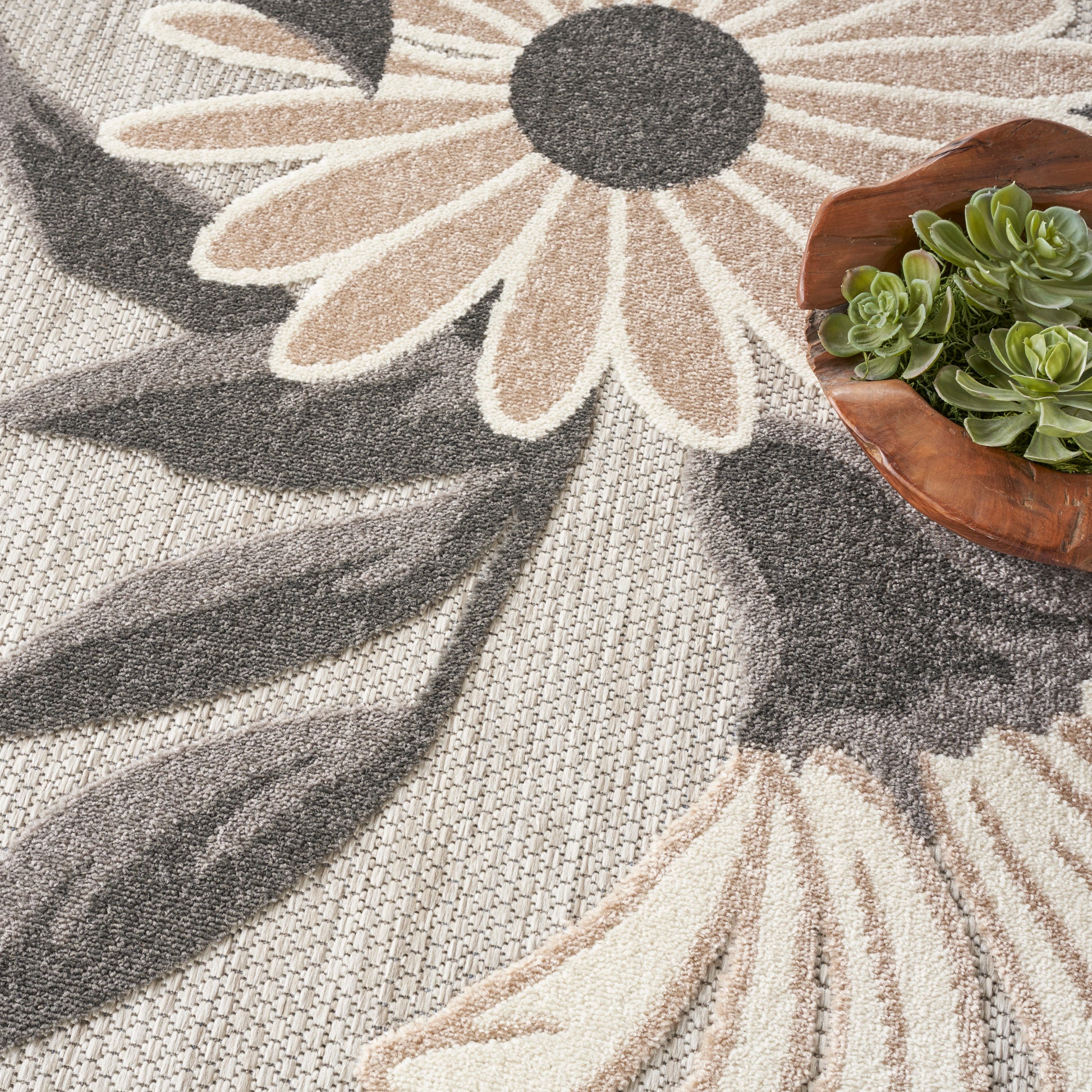 Neutral daisy-pattern 8' round rug in beige, taupe and gray; small wooden bowl with green succulents.